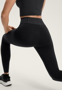 Crne helanke od rastezljivog materijala, s visokim pojasom i elegantnim, tijesno pristajućim dizajnom bez vidljivih uzoraka ili naglasaka.