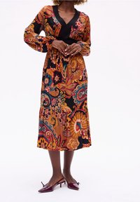 Robe midi à imprimé floral marron, avec des manches longues, un décolleté en V et une taille cintrée. Associée à des talons aiguilles bordeaux.