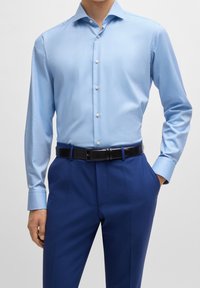 Jasnoniebieska koszula na długi rękaw z kołnierzykiem w szpic, z białymi guzikami i gładką fakturą, w połączeniu z granatowymi spodniami i czarnym paskiem.