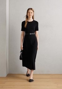 Melnā midi kleita ar īsām piedurknēm, savilktā jostas daļa, mīksts audums. Apvienota ar melnajām kurpēm plakanā zolē, uz kurām ir dekoratīvs raksts, un mazu roku somiņu.