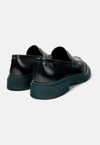 Svarta läderslip-on skor med en slät yta, med en mörkgrön gummisula och subtil märkning på hälen.