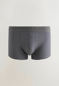 Tumši pelēki bokseršorti, kas izgatavoti no mīksta auduma ar tekstūru elastīgu jostasvietu, uz kuras atkārtoti ir rakstīts vārds "NĀKAMAIS".