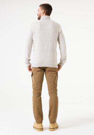 Knitted light gray high-neck sweater, textured with a ribbed hem, paired with tan cargo pants and tan shoes, viewed from behind.