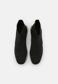 Svarta slip-on-skor med en texturerad vävd ovandel, utrustade med en hög ankel-design och vit gummisula. Märkningen syns på insidan.