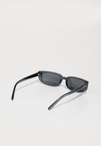 Lunettes de soleil rectangulaires noires avec des verres foncés et une monture en plastique brillant. Présente des branches fines avec une marque sur le côté.