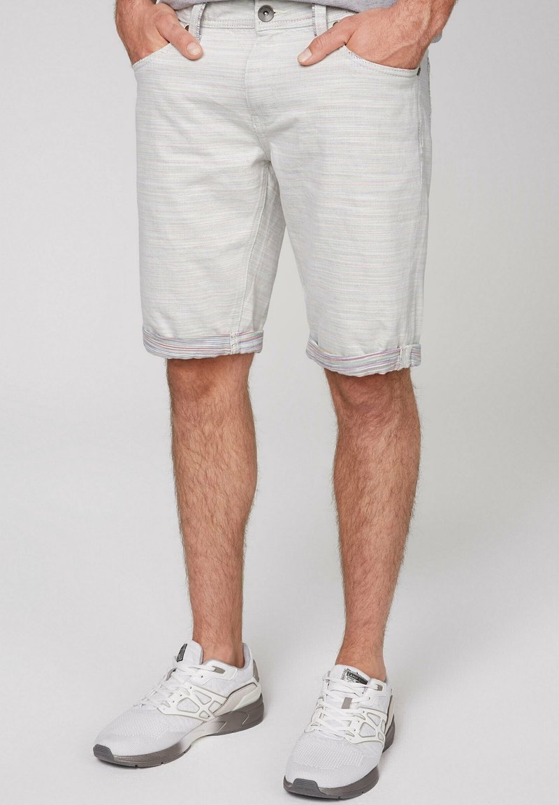 Shorts en denim gris clair avec un motif rayé subtil, ourlet roulé et poches avant. Associés à des chaussures de sport blanches.