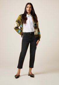 Cárdigan de punto con un patrón en verde y azul, camisa blanca de botones, vaqueros negros de pierna recta y bailarinas negras con un acento estampado.