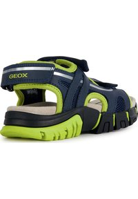 Navy and bright green sandals with adjustable straps, mesh inserts, and a cushioned sole. Features a grooved black and green outsole.