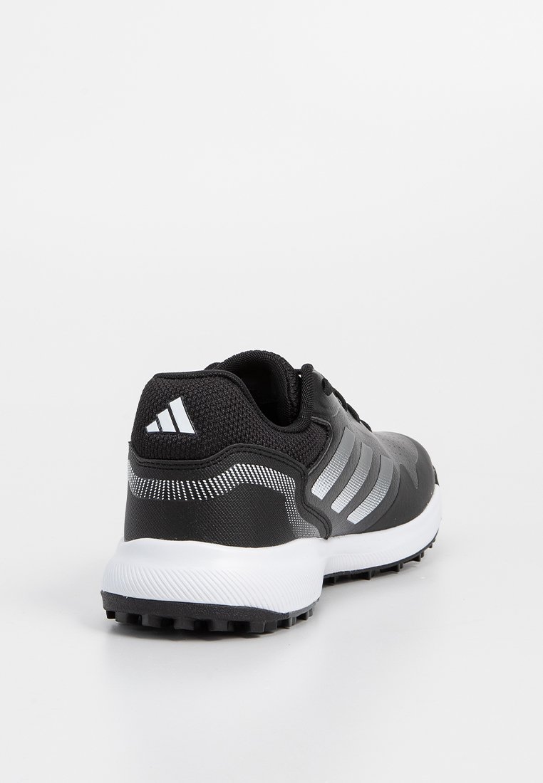 Chaussure de sport noire avec un dessus texturé, trois rayures argentées brillantes, une semelle épaisse blanche et une semelle extérieure en caoutchouc noir à traction.