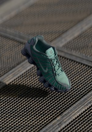 Roheline sneaker, millel on võrgu ülemine osa ja kummist tald, silmapaistva tekstuuriga disain ning silmapaistvad pehmendavad detailid kanna lähedal.