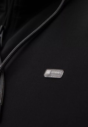 Musta kangas, jossa on sileä pinta, harmaa vetoketju ja muovinen logo-etiketti, jossa on sana "ombre" selvällä kirjoituksella.