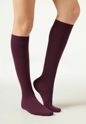 Burgunderfarbene kniehohe Socken aus einem weichen, glatten Material mit gerippten Bündchen und einem nahtlosen Zehenbereich.