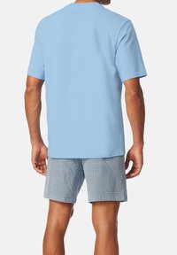 Hellblaue Baumwoll-T-Shirt mit kurzen Ärmeln, kombiniert mit gemusterten Shorts in Navy und Weiß mit geometrischen Designs.