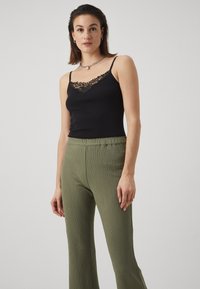 Black camisole with lace trim, paired with olive green textured wide-leg pants. Both items feature a fitted silhouette and delicate detailing.