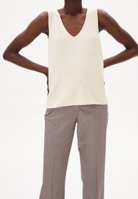 Kermanvärinen hihaton toppi V-pääntiellä ja kuvioidulla kankaalla, yhdistetty ruskeisiin ja valkoisiin ruudullisiin housuihin, joissa suorat lahkeet ja sivutaskut.