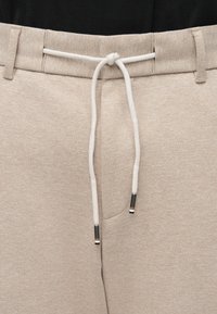 Béžové teplákové nohavice s textúrovaným povrchom, vybavené pásom na šnúrku s čierno-bielymi koncami a dvoma bočnými vreckami.