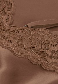 Brun satinfabric med intrikata spetsdetaljer som har blommönster längs kanten. Slät textur med en glänsande yta.