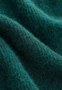 Țesătură de lână verde închis, cu o textură moale și pufoasă, prezentând un model delicat de valuri și o ușoară strălucire, care evidențiază adâncimea și bogăția.