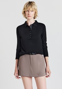 Polo noir à manches longues avec un patte de boutonnage, associé à une mini-jupe marron avec des plis devant et une ceinture noire.
