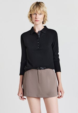 Polo shirt nero a maniche lunghe con abbottonatura, abbinato a una mini gonna marrone con pieghe frontali e una cintura nera.
