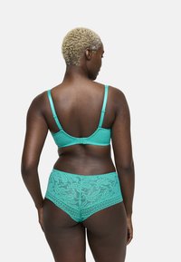 Reggiseno in pizzo turchese e mutandine a vita alta. Presenta motivi floreali, spalline regolabili e una chiusura a gancio sul retro.