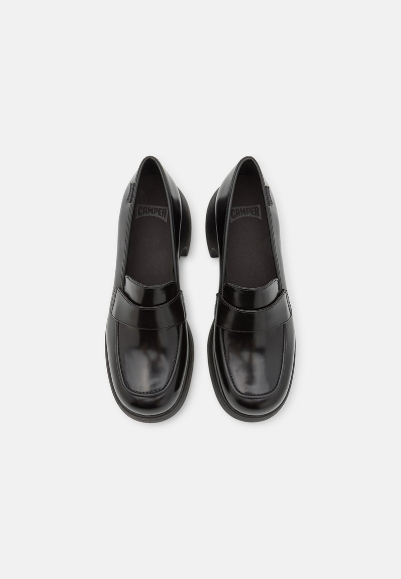 Mocassins en cuir noir avec un bout arrondi, accent de sangle et semelle en caoutchouc. Texture lisse avec une finition brillante. Logo CAMPer visible à l'intérieur.