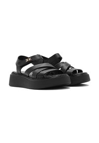 Sandali in pelle nera con cinturini larghi e retro regolabile. Presentano una suola platform nera spessa e un sottile dettaglio in oro con il logo.