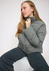 Gray puffer jacket with a high collar, featuring a smooth, shiny texture and zip closure, paired with dark corduroy pants.