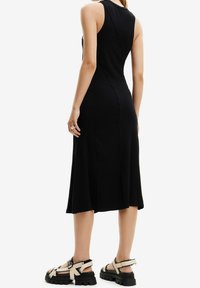 Musta, ribbineulottu midimekko, jossa on vartalonmyötäinen siluetti ja sivuhalkiot; yhdistetty paksupohjaisiin mustiin sandaaleihin, joissa on beigej�ä hihnoja ja säädettävä solki.