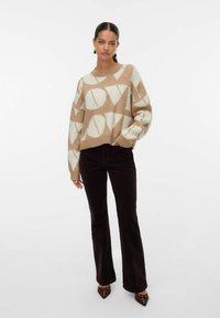Pull brun et crème avec un graphique "LOVE" audacieux, col rond et coupe ample, associé à un pantalon large foncé et des escarpins à bout pointu.