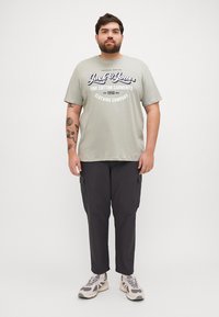 Hele rohelise puuvillase T-särgiga, millel on "Jack & Jones" graafika, koos tumedate kargo pükstega, millel on küljetaskud ja heledate spordijalatsitega.