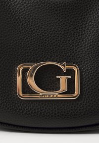 Borsa a tracolla in pelle nera dalla texture ampia, con un prominente logo "G" in tono oro all'interno di un quadrato delineato, che mette in risalto un design elegante.