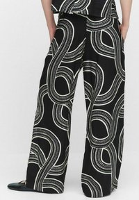 Breda byxor i svart tyg med ett vitt abstrakt swirl-mönster. Slät textur med resårmidja för komfort.