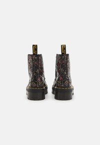 Czarne kwiatowe botki za kostkę z teksturowanym wykończeniem, wyposażone w masywną podeszwę, kontrastujące żółte przeszycia oraz pętelki do łatwiejszego zakładania.