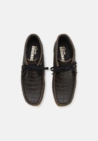 Zwarte leren schoenen met een krokodillenleer textuur, ronde neus en veters. De binnenvoering heeft het "Clarks ORIGINALS" merkteken.