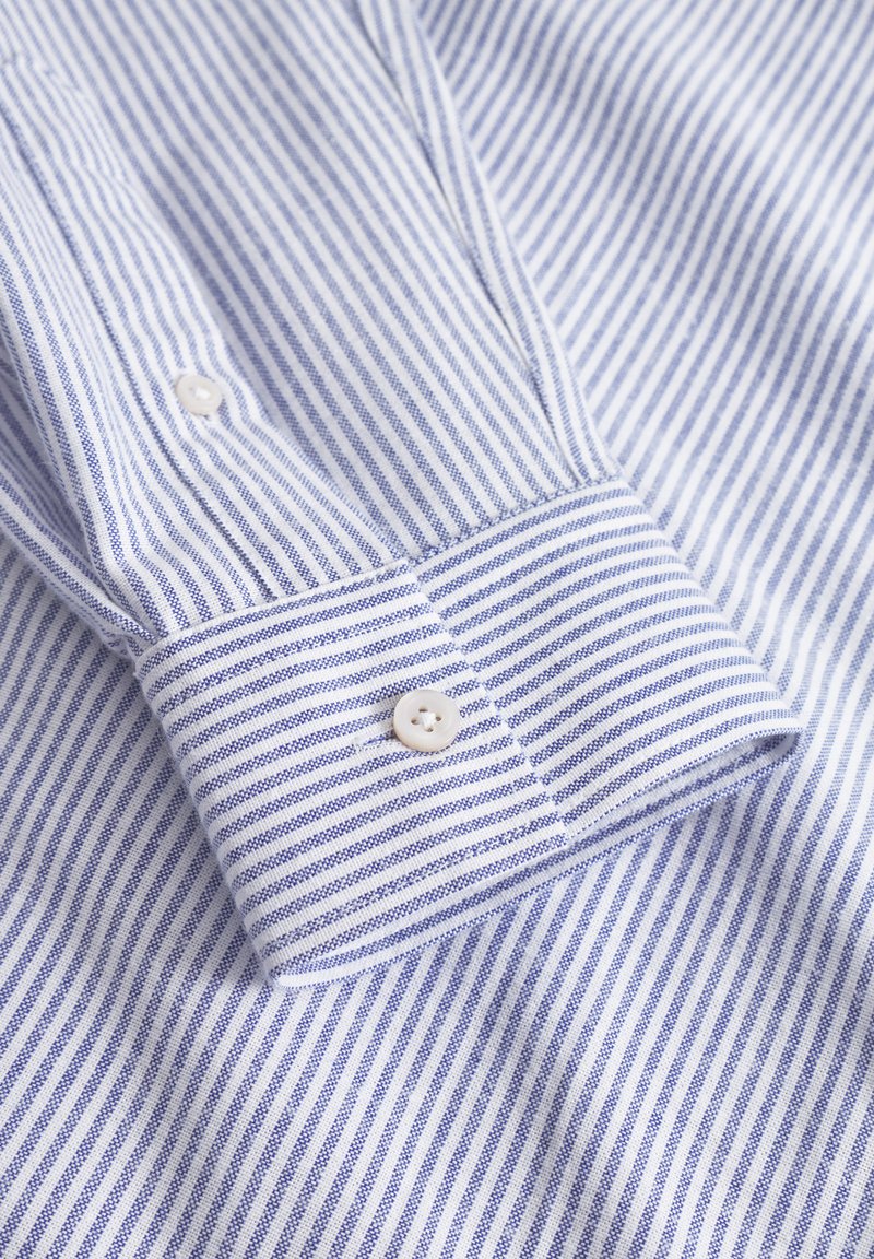 Puño de camisa a rayas en azul claro y blanco. Tejido de algodón, con finas rayas verticales, dos cierres de botón blancos y un diseño ajustado.