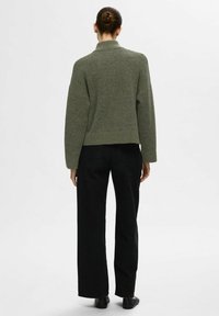 Pull en maille vert olive avec un col montant et des épaules décontractées, associé à un jean noir à jambes larges. Design simple, texture douce et sans motifs.