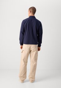 Navy windbreaker with elastic cuffs and collar, paired with beige cargo pants featuring side pockets and a patch near the waistband.