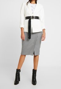 Vit kavaj med uppkavlade ärmar, svart tygbälte med en cirkulär spänne, i kombination med en knä-lång svart och vit houndstooth pennkjol och svarta ankelstövlar.