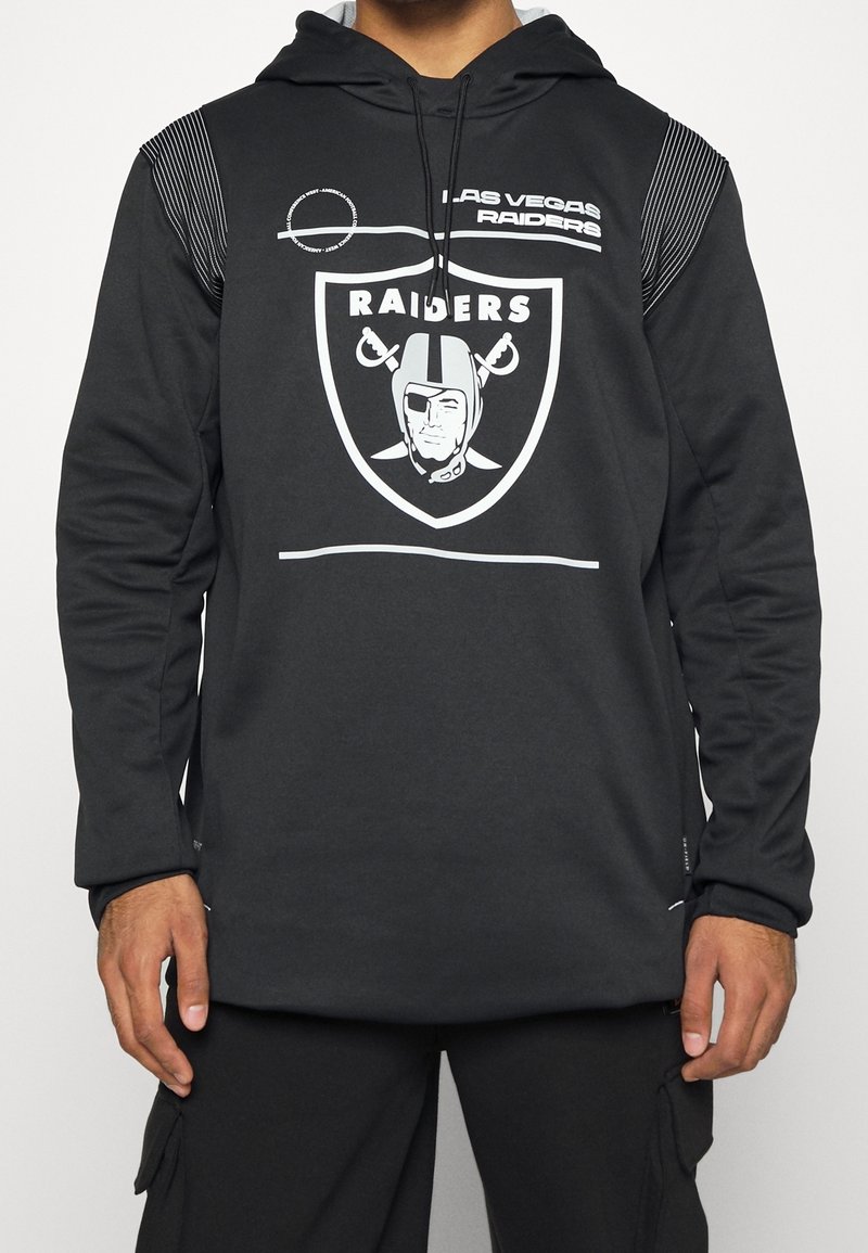 Černá mikina s hladkým materiálem má velké logo Raiders, bílé akcenty a pruhovaný design na ramenou. Dlouhé rukávy.