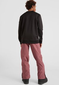 Zwarte sweater met lange mouwen en ronde hals, gecombineerd met roze sneeuwbroeken met ritsen en een relaxte pasvorm. Zwarte schoenen maken de look af.