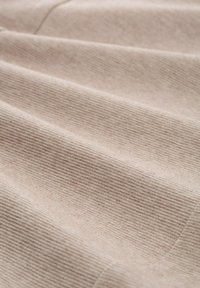 Tessuto beige chiaro con una sottile texture a coste, che mostra morbide pieghe e una finitura liscia, ideale per applicazioni di tappezzeria o moda.