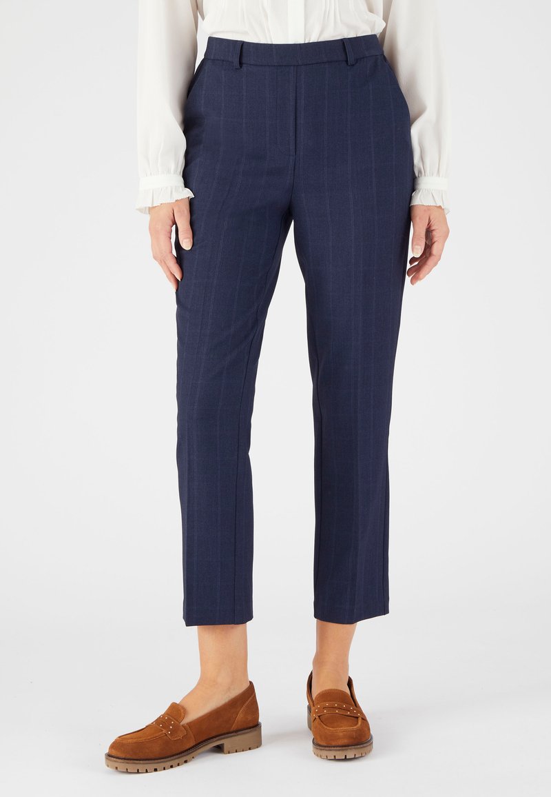 Marineblauwe pinstripe broek met een getailleerde pasvorm, voorzien van een platte voorkant en zijzakken. Gecombineerd met bruin suède instappers.
