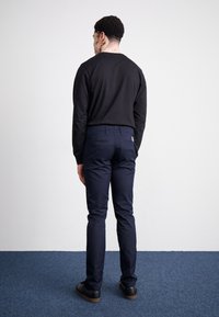 Chemise noire à manches longues associée à un pantalon bleu marine. Le pantalon a deux poches arrière, avec une coupe ajustée et une texture lisse.