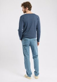 Camicia a maniche lunghe a righe blu con scollo tondo, abbinata a pantaloni blu chiaro con due tasche posteriori e sneakers beige.