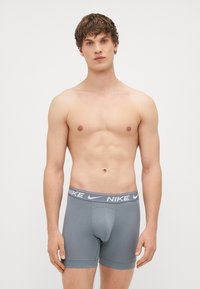 Pelēki kokvilnas boksershorts ar pieguļošu dizainu un elastīgu jostu, kurai ir Nike logo baltā krāsā. Gluda tekstūra, garums līdz vidussmēra augšstilbam.