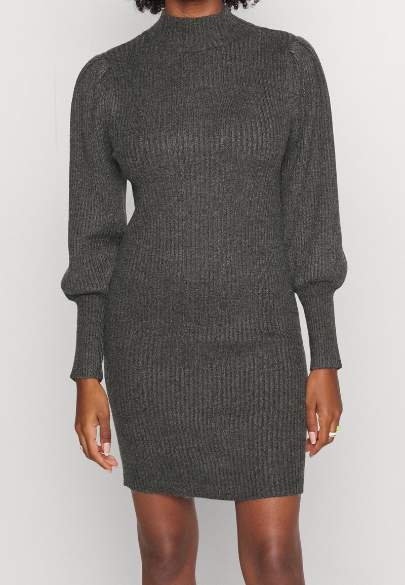 Robe en maille côtelée gris foncé avec manches longues bouffantes et col montant, portée par une personne debout sur un fond uni.