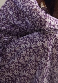 Un tissu violet arbore un motif floral en blanc, avec une texture fluide et des motifs délicats. Le matériau semble léger et doux.