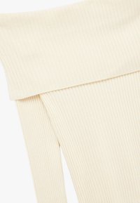 Geripptes, off-white Stoff mit einer weichen, strukturierten Oberfläche; verfügt über einen breiten gefalteten Bund an der Oberseite für einen sicheren Sitz und angenehmen Tragekomfort.