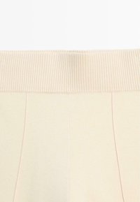 Jasnobeżowy prążkowany pas z gładką, miękką fakturą. Tkanina przechodzi w płaską, jasnobeżową powierzchnię z subtelnymi detalami szwów.